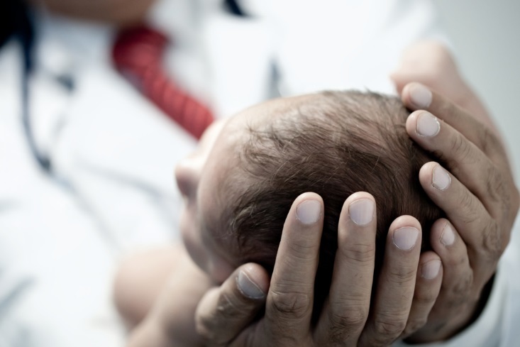 Der Kinderarzt hält das Köpfchen des Neugeborenen in seinen Händen. 

[Copyright = ESB Professional / shutterstock.com]