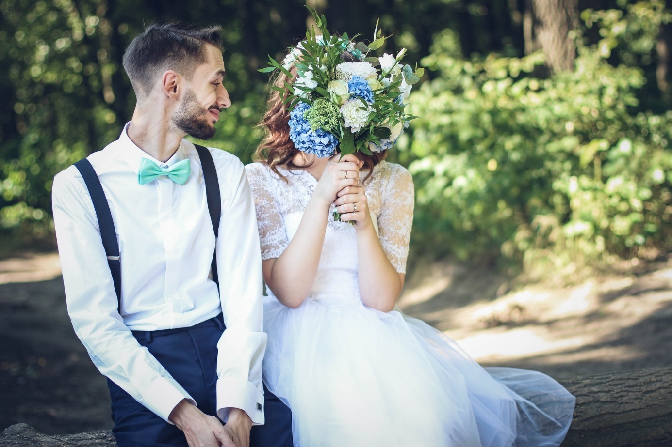 Bräutigam mit Braut, die sich Blumenstrauß vor das Gesicht hält. 