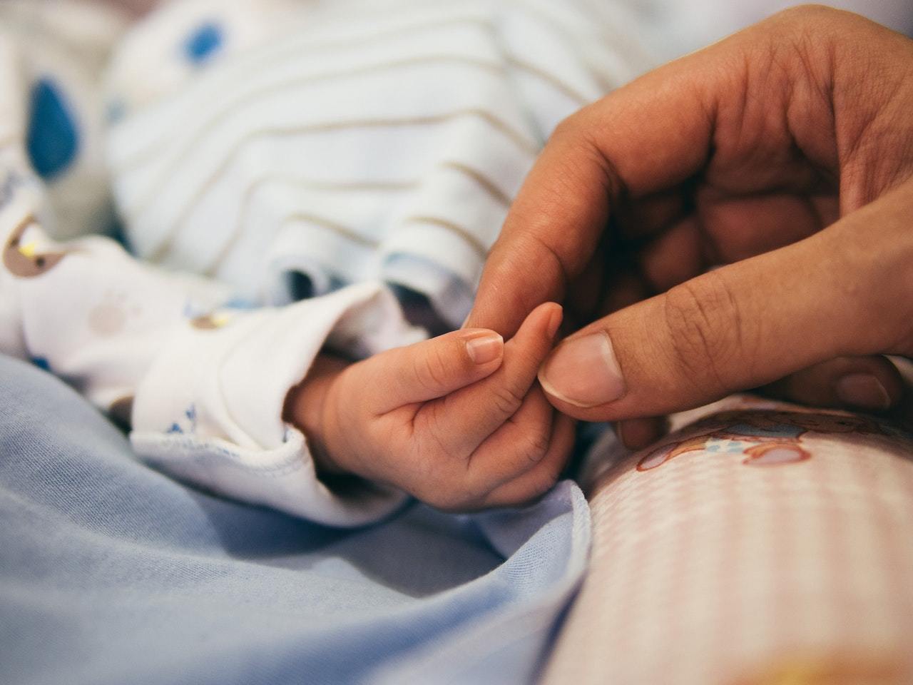 Eine große Hand hält die winzige Hand eines Neugeborenen.