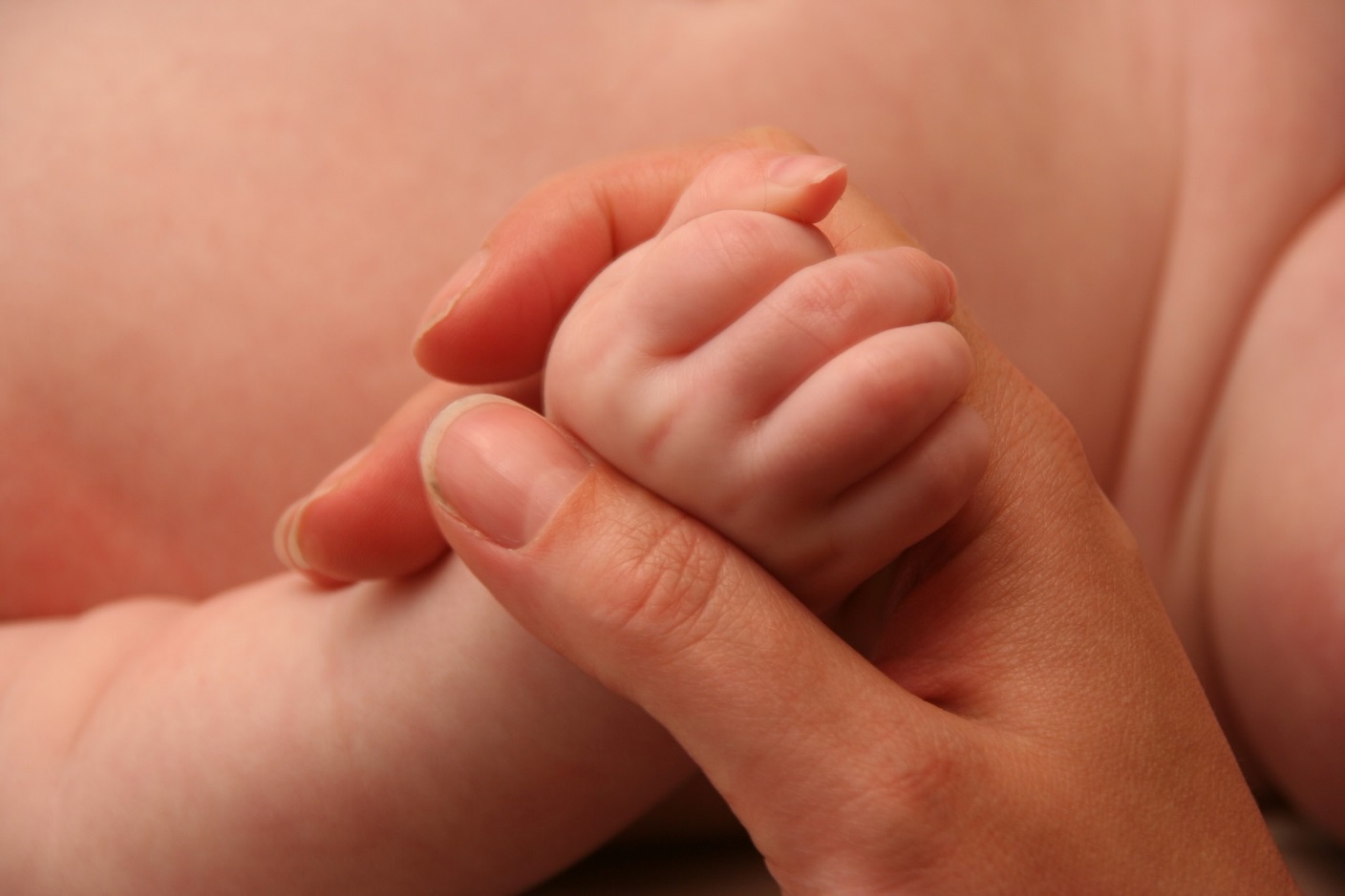 Die Hand der Mutter umarmt eine kleine Babyhand.