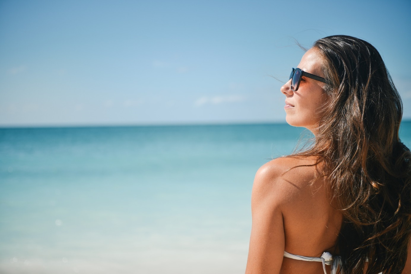 Frau mit Sonnenbrille am Meer unter blauem Himmel.