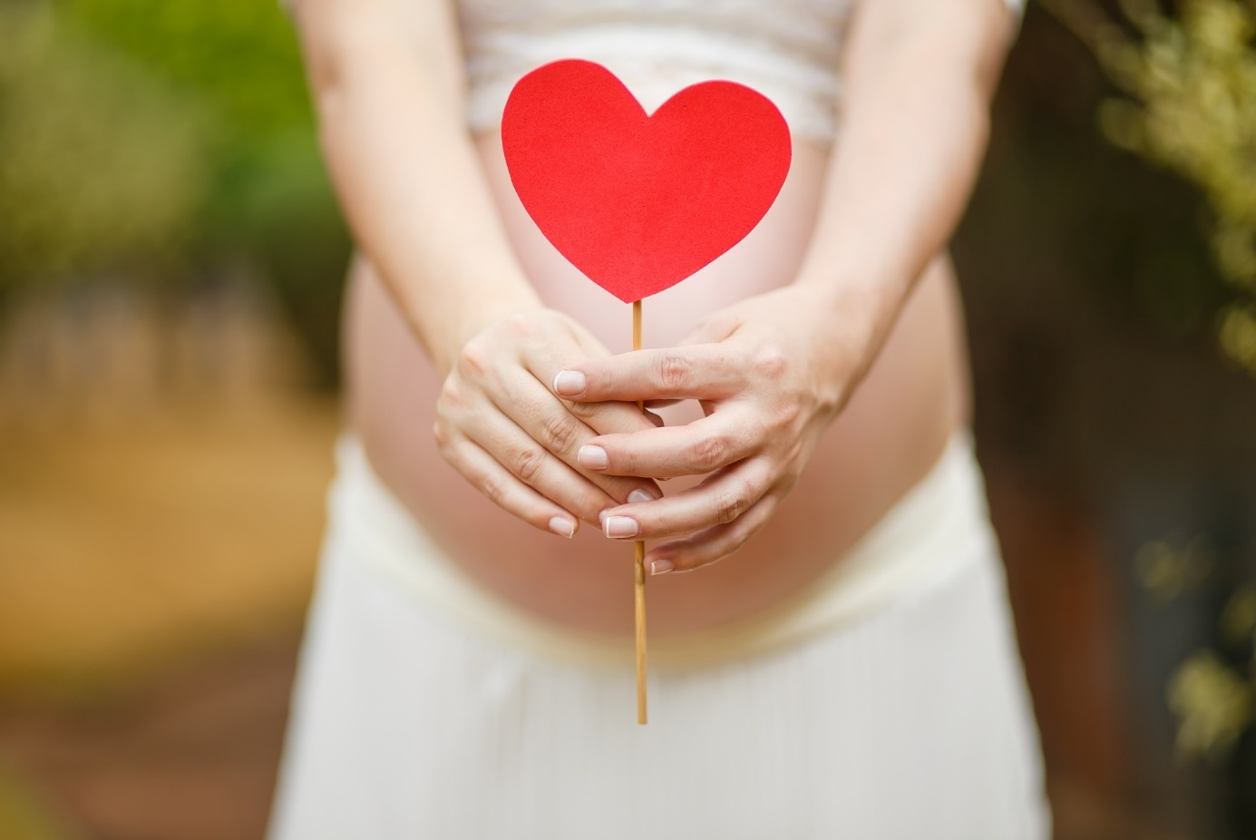 Schwangere hält ein Herz aus Pappe vor ihren Bauch. 